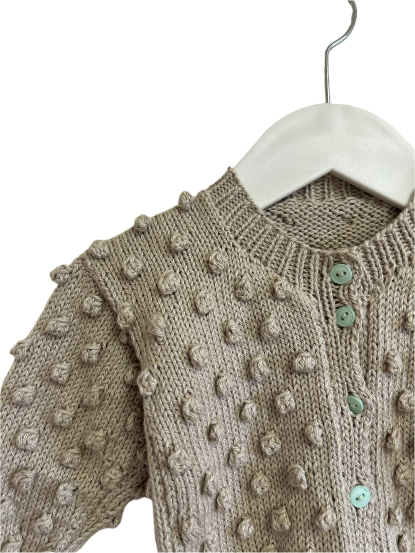 Knitted sweater with textured pattern and green buttons on a hanger against a neutral background