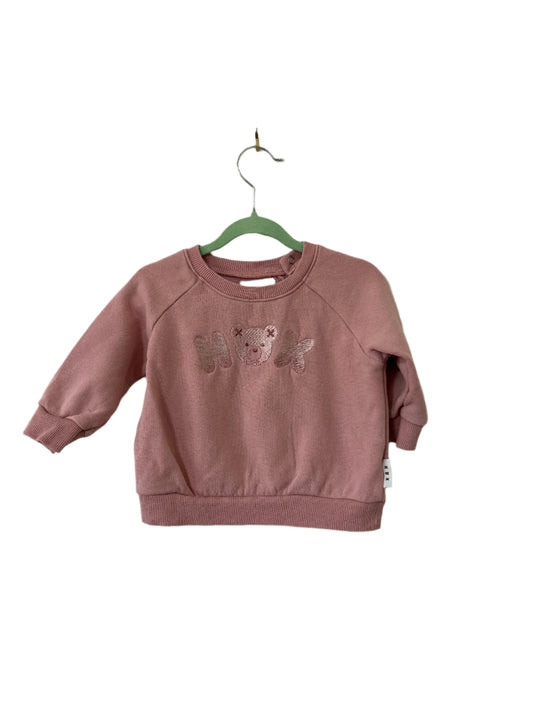 Pink sweatshirt with teddy bear design on a hanger against a plain wall