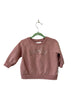Pink sweatshirt with teddy bear design on a hanger against a plain wall