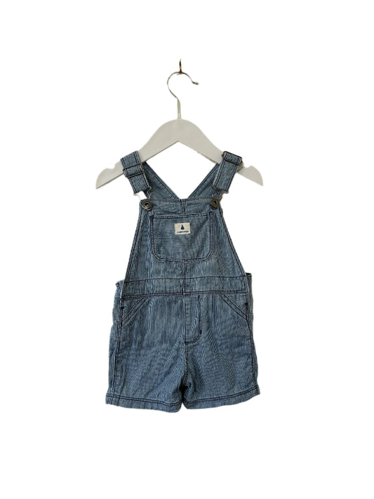 Blue denim overalls hanging on a white hanger against a beige wall