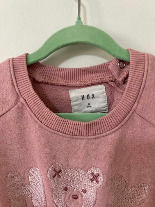 Pink sweatshirt with teddy bear design on a hanger against a plain wall